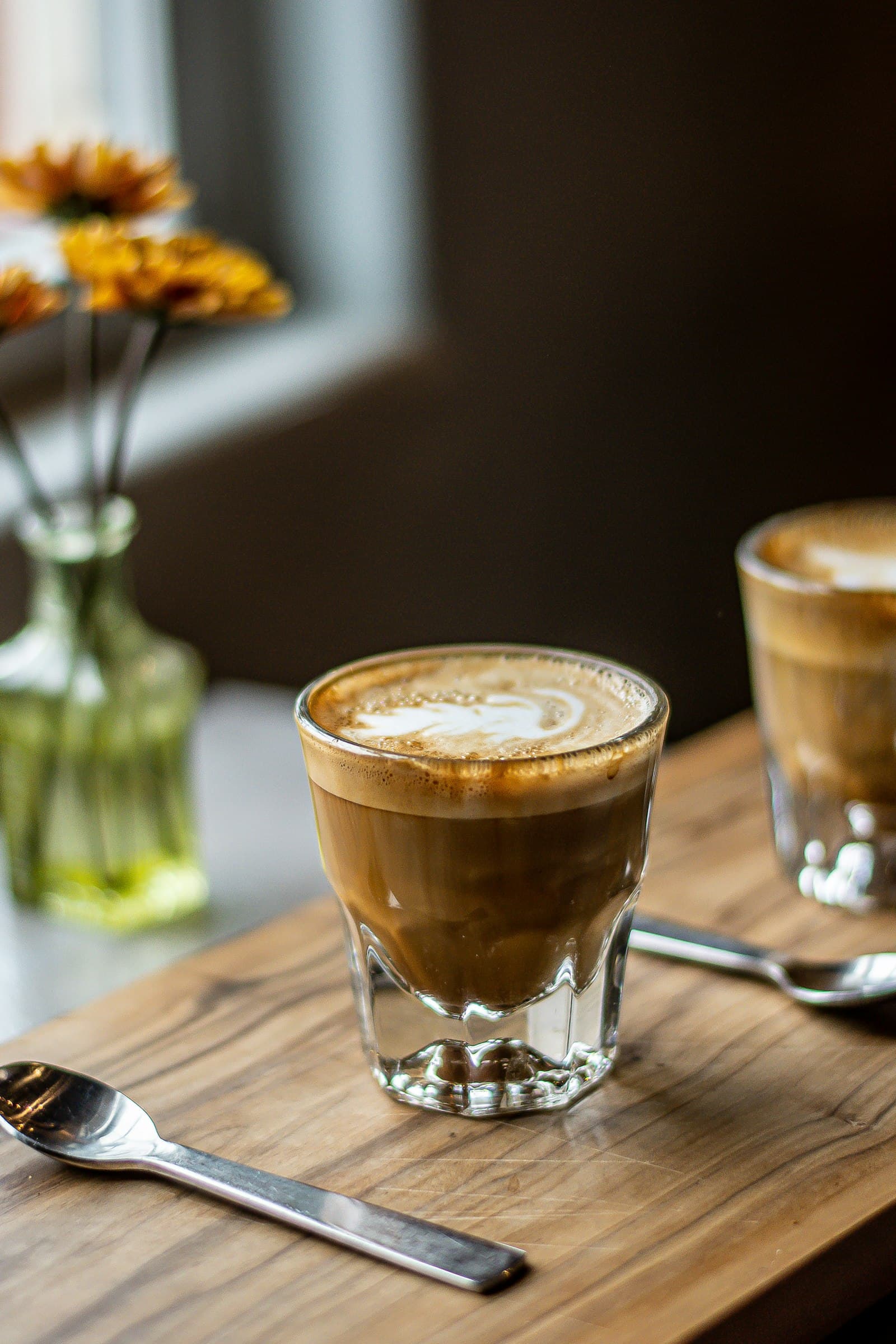 A cortado in a small glass on a wooden board