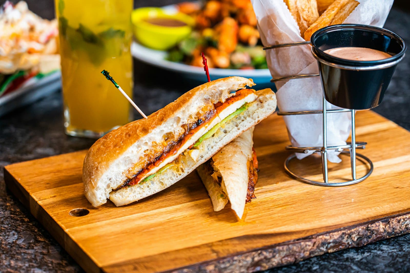 A pressed sandwich cut in half on a board, with yuca fries