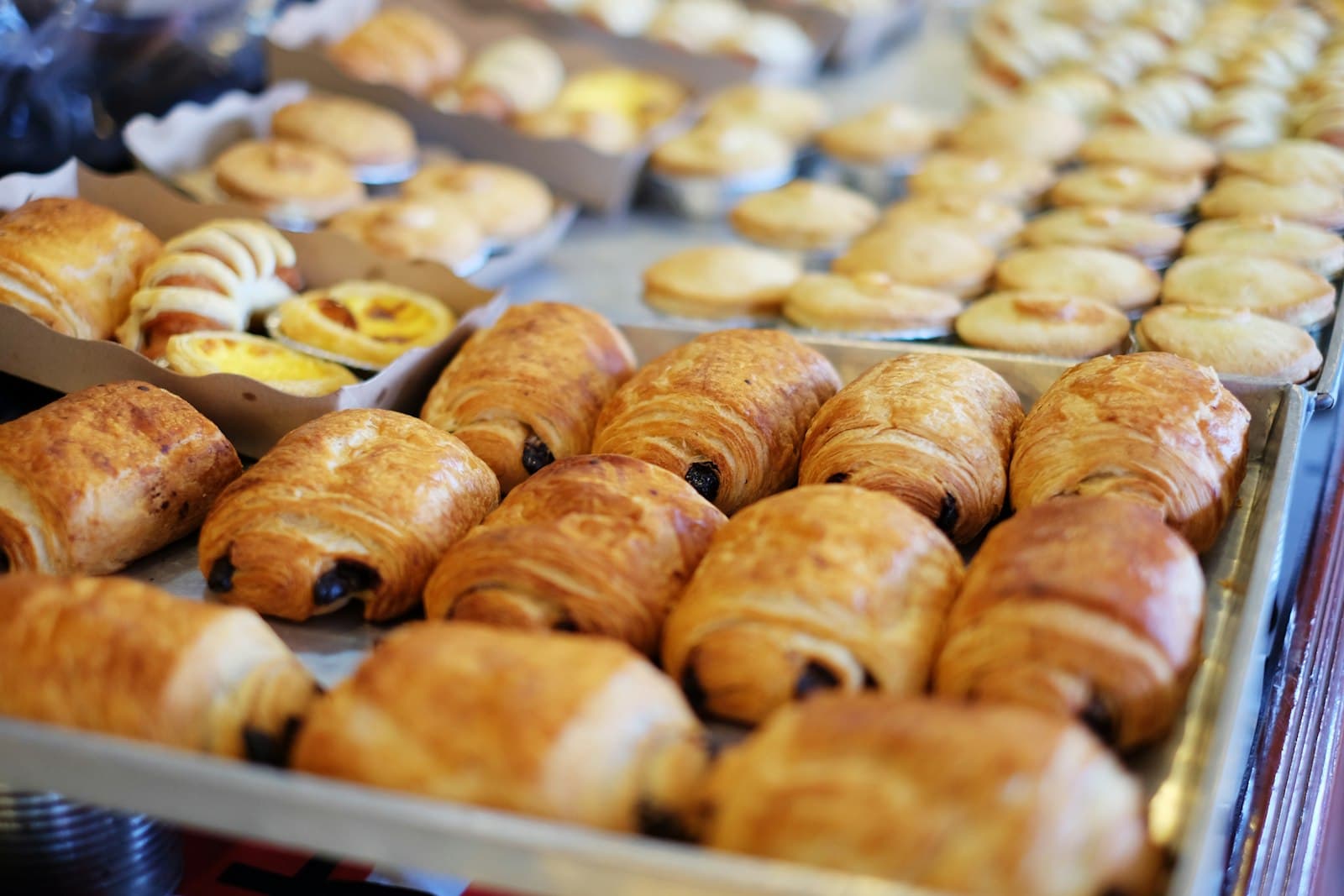 A tray of chocolate croissants beside custard tarts