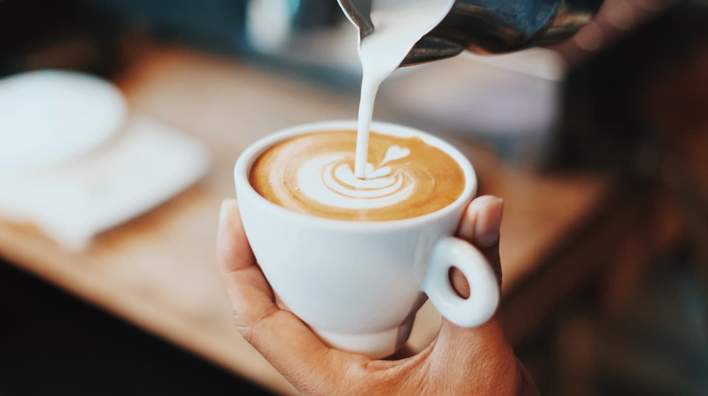 Milk poured into a latte in a white cup held over the bar