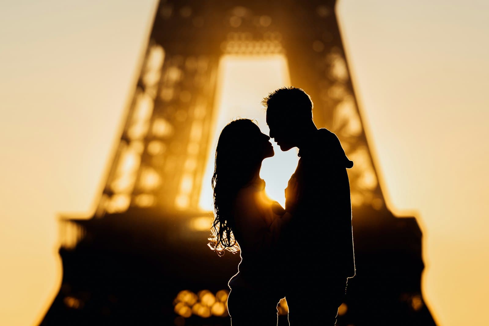 Silhouette of a couple about to kiss under the Eiffel Tower in golden light
