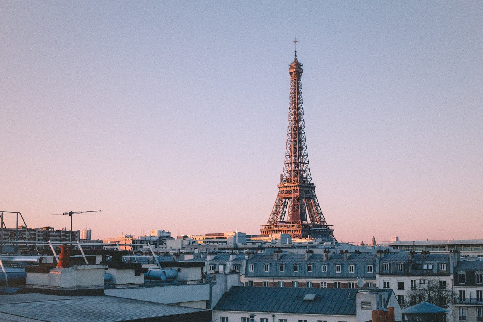 The Eiffel Tower over Paris rooftops under a pink dawn sky