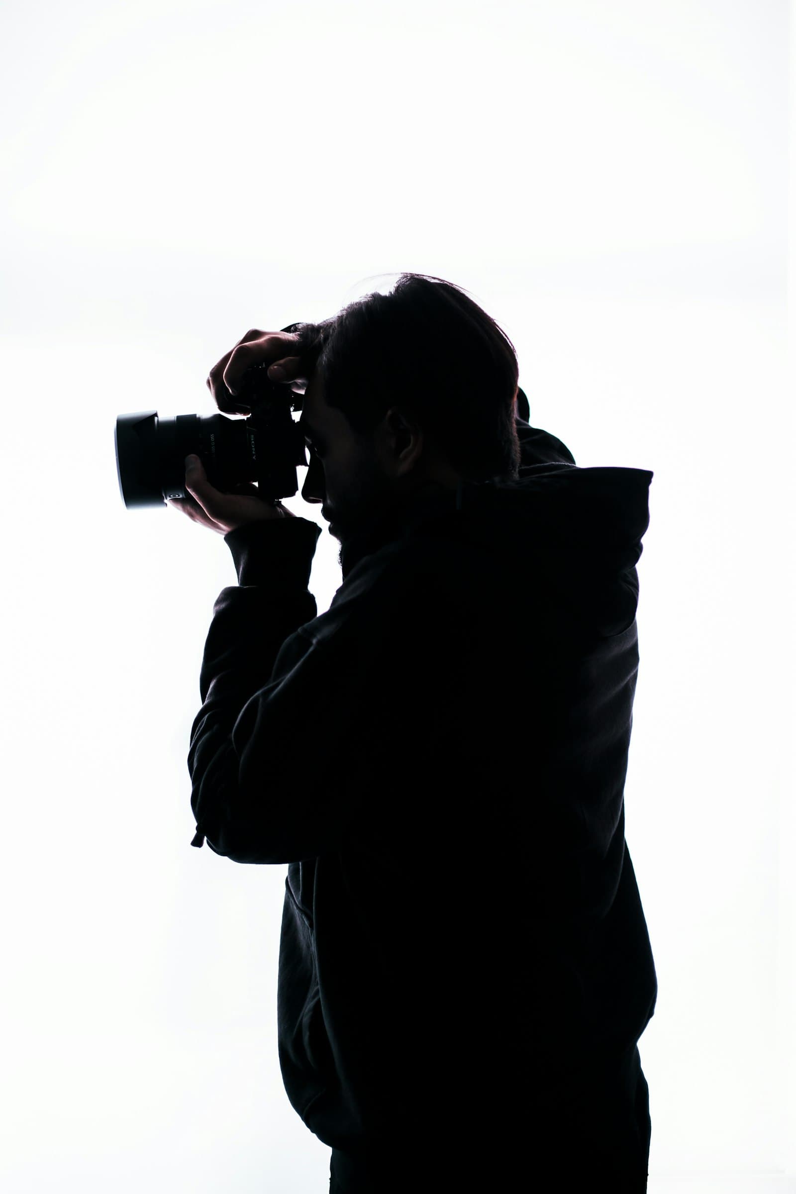 Silhouette of a photographer raising a camera against a white background