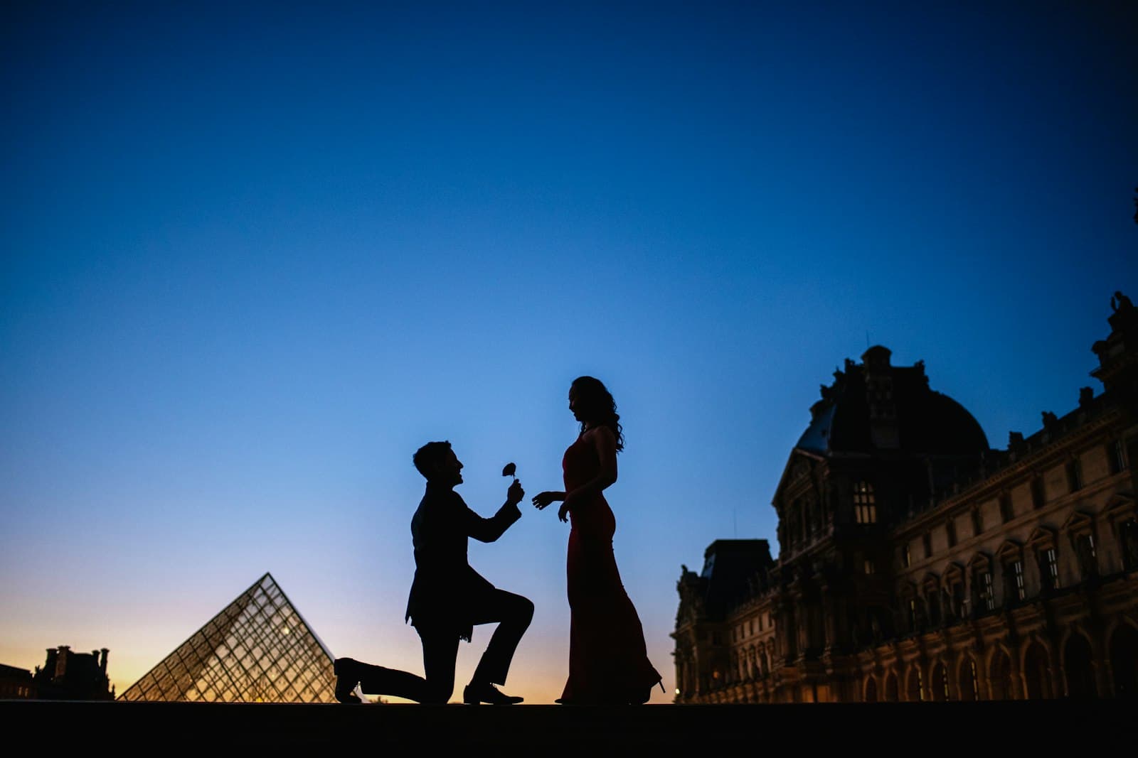 Silhouette of a proposal in front of the Louvre pyramid at dusk