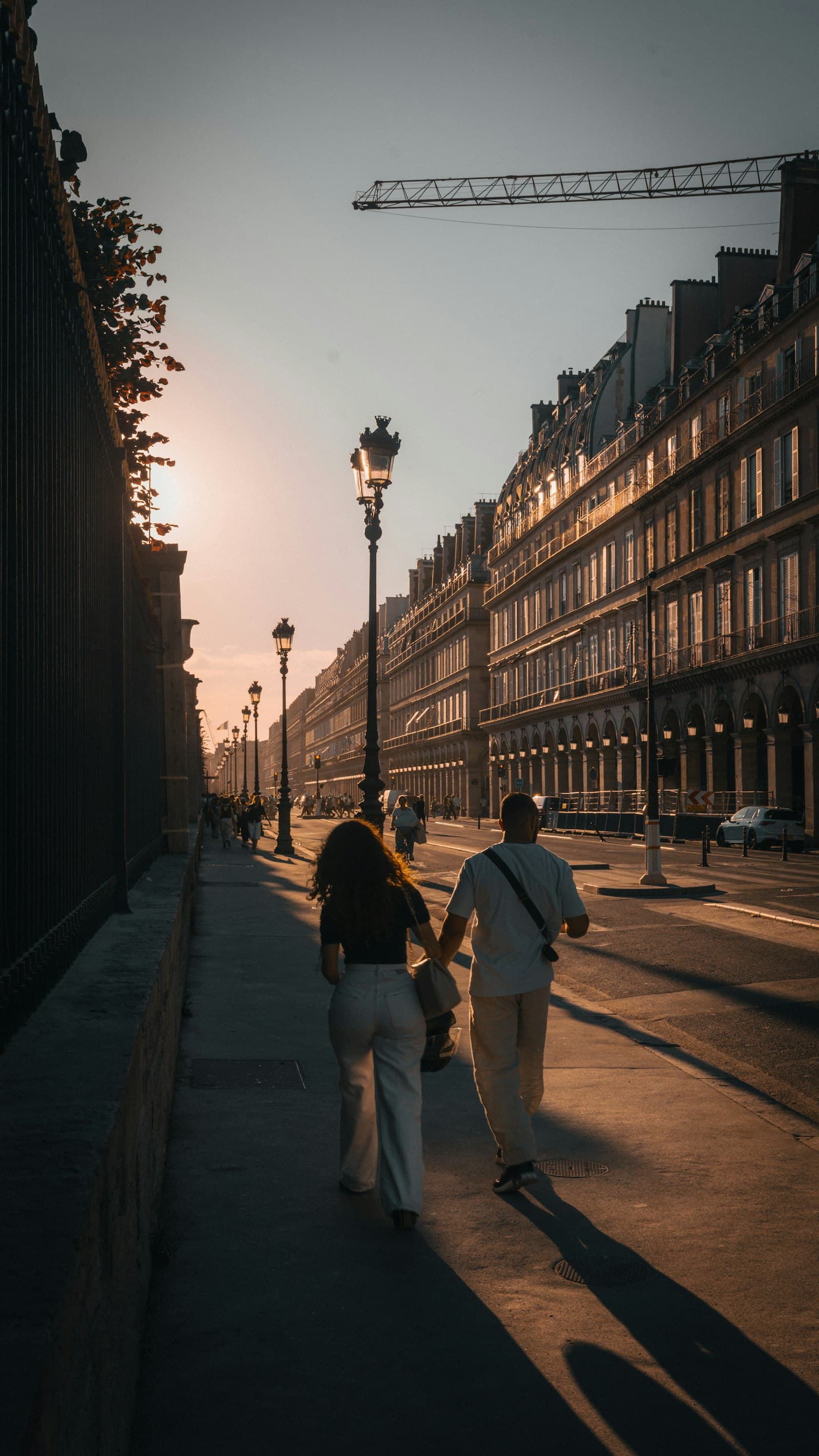 A couple walking hand in hand beside the Tuileries railings at golden hour