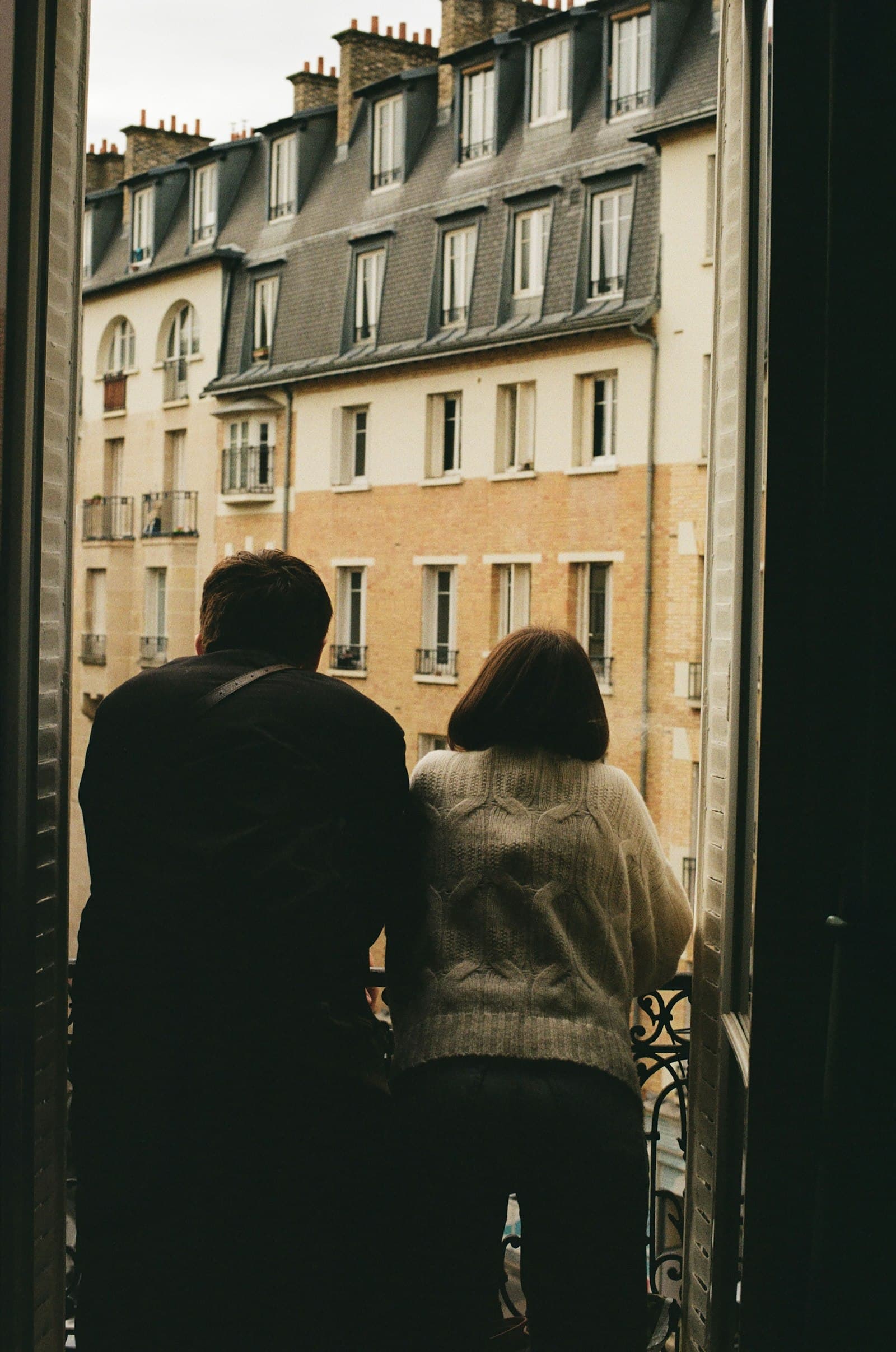 A couple at an open window, looking across at Paris apartment buildings