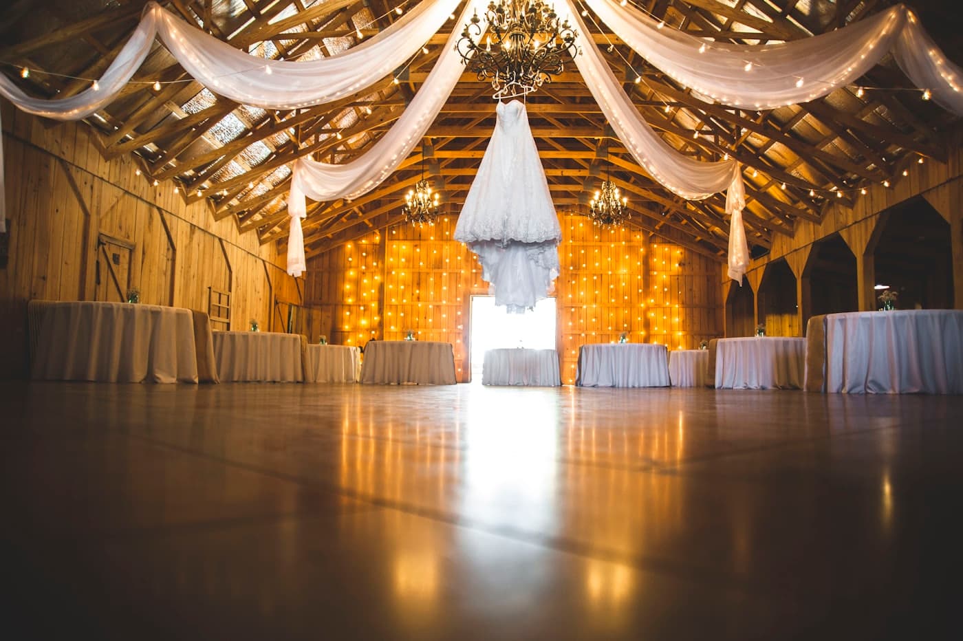 The barn interior draped in ivory fabric, with string lights, chandeliers and round tables