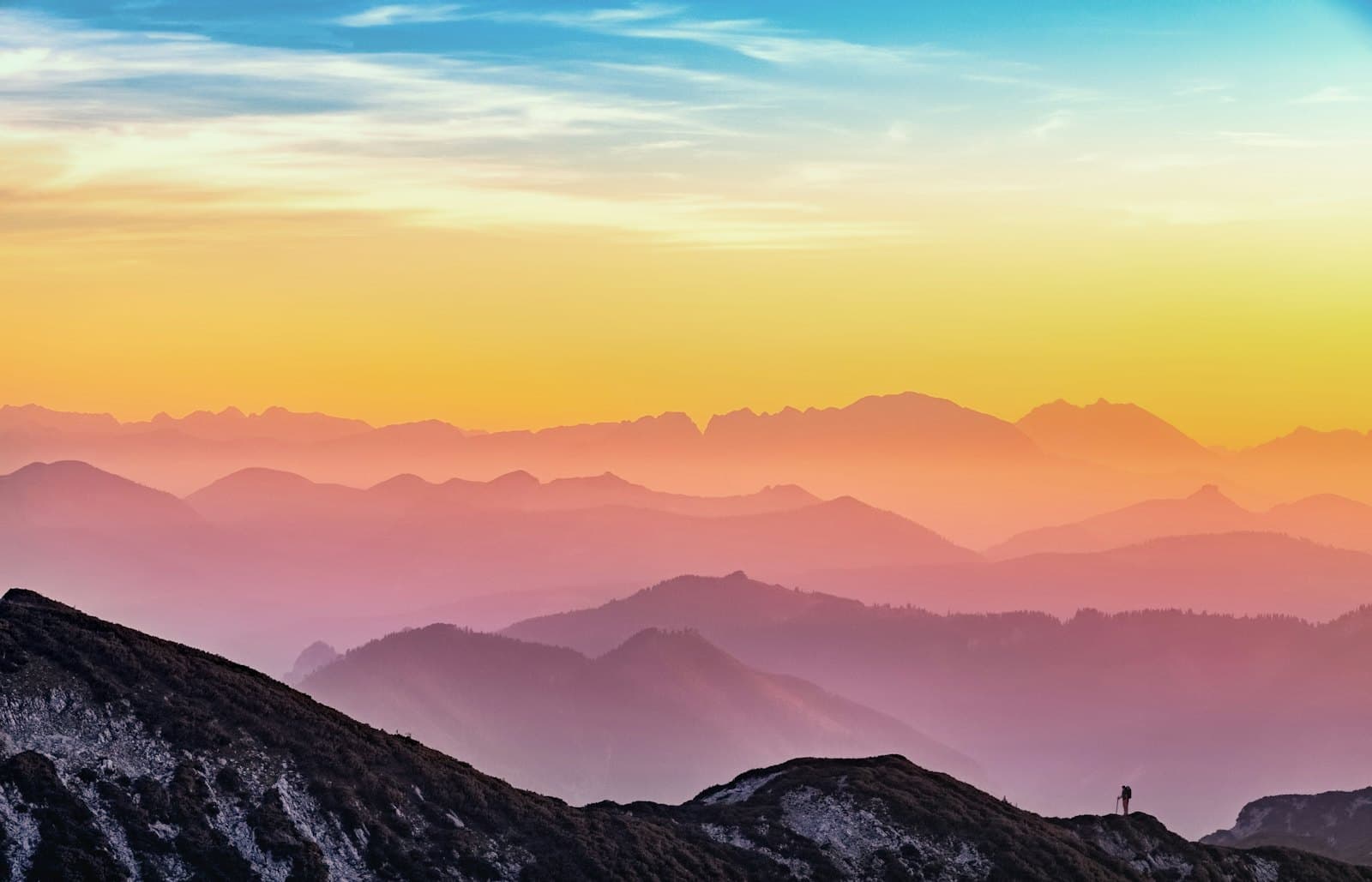 Layered mountain ridgelines fading into orange and violet haze at sunset