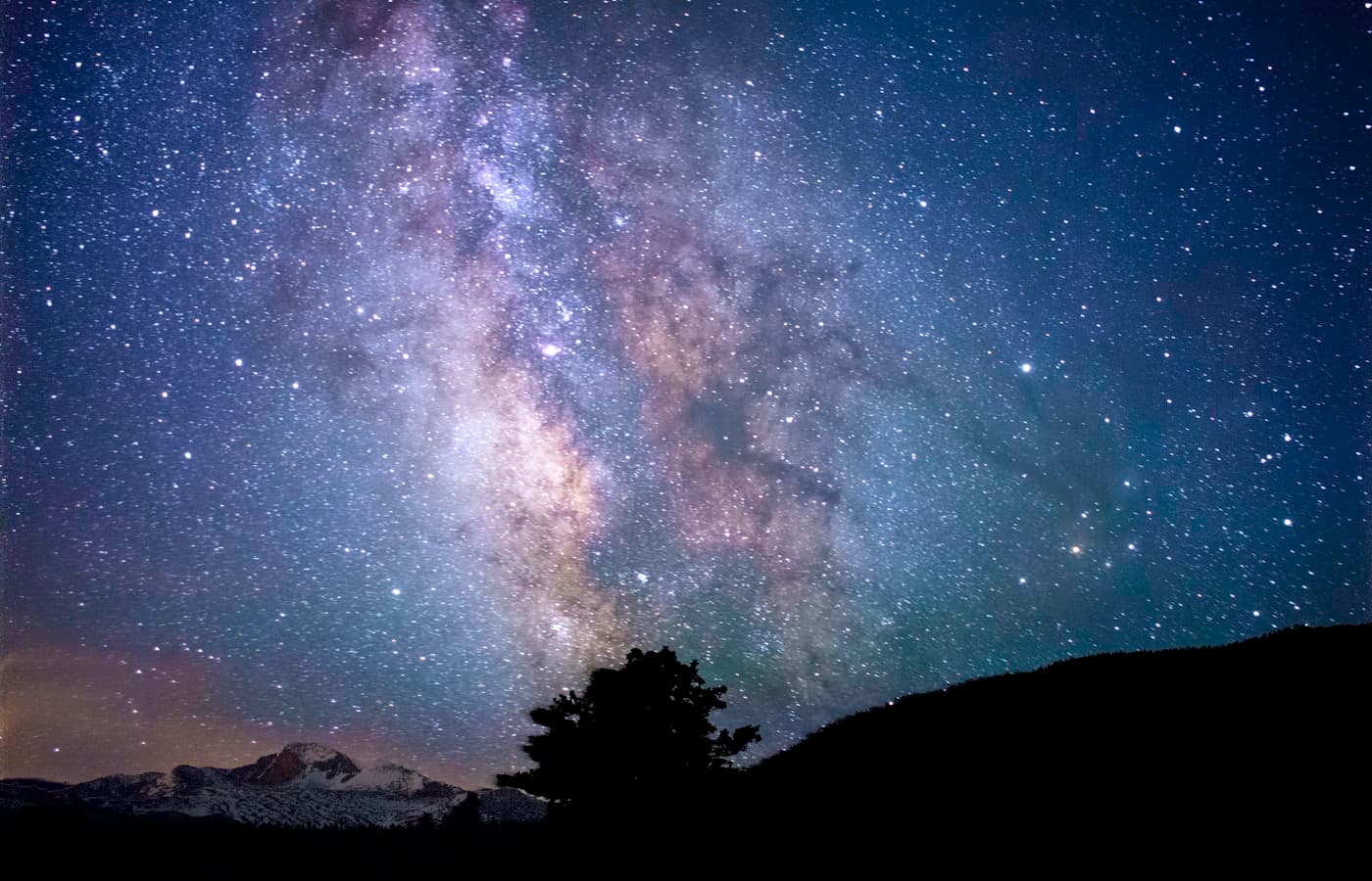 The Milky Way over a dark mountain ridge and a lone silhouetted tree