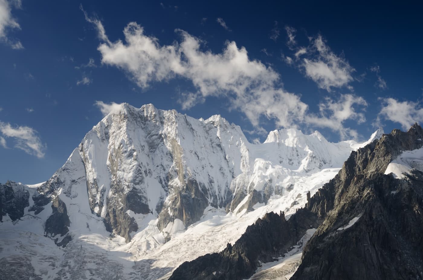 Snow-plastered alpine headwall and glacier under a deep blue sky with drifting clouds