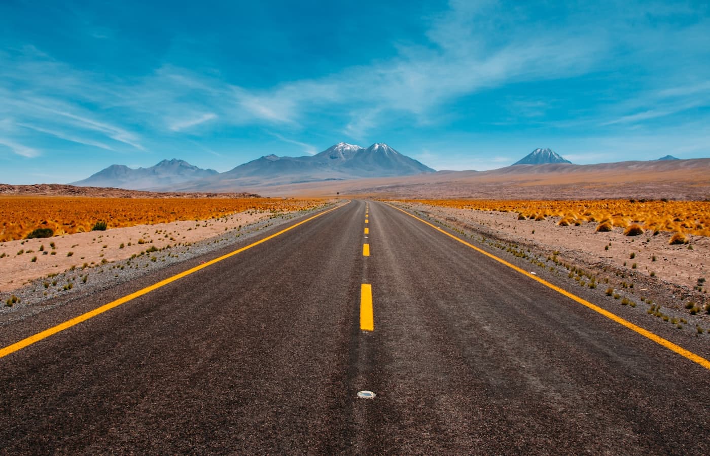 Empty desert two-lane highway running straight toward snow-capped volcanoes