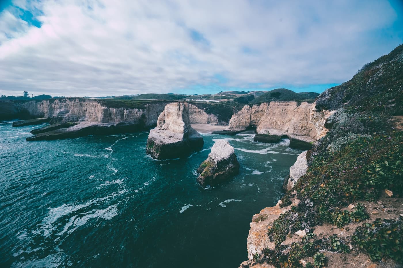 Turquoise cove with pale cliffs and offshore sea stacks under a clouded sky