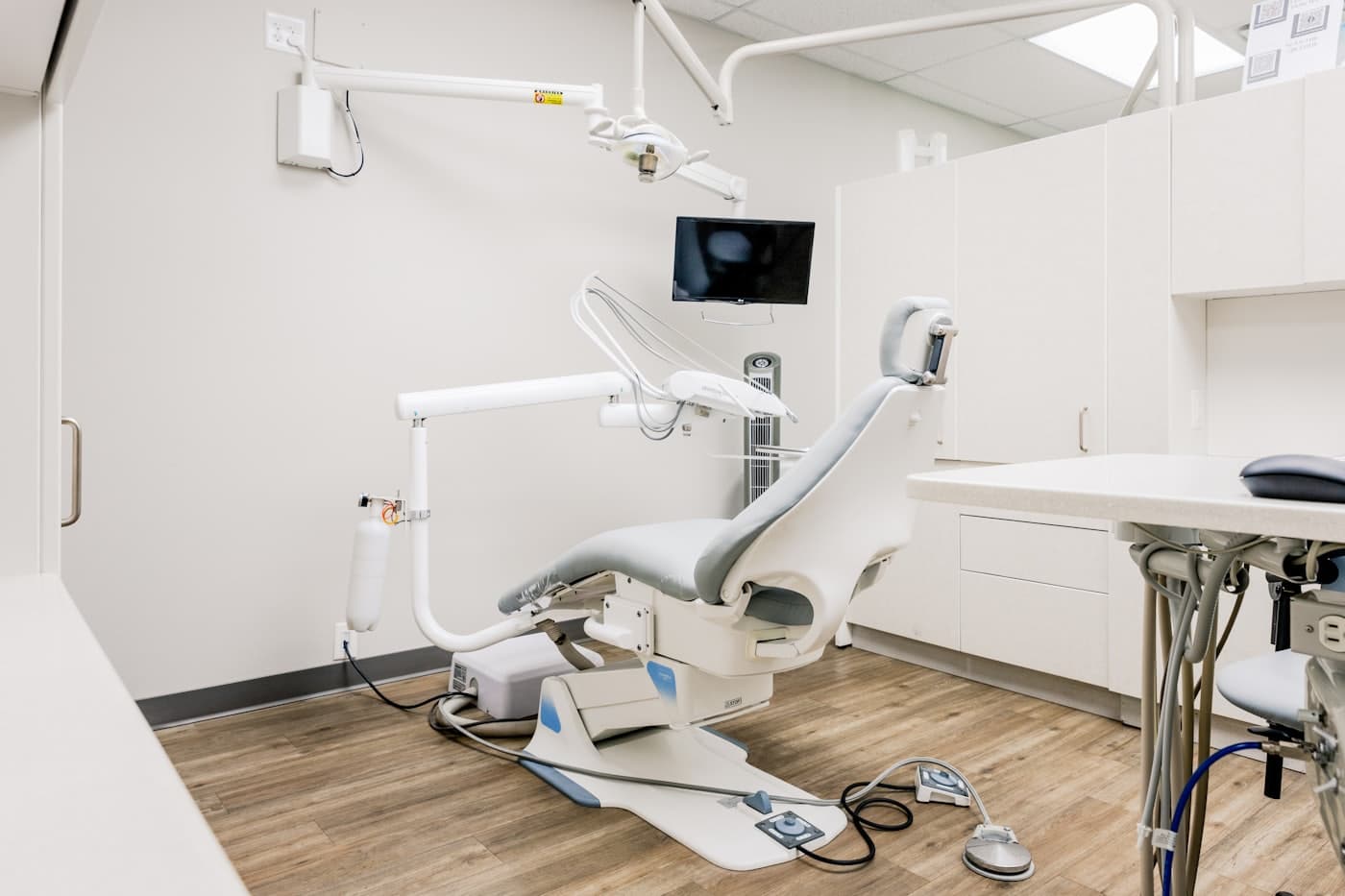Calm treatment room with warm wood flooring and a grey patient chair