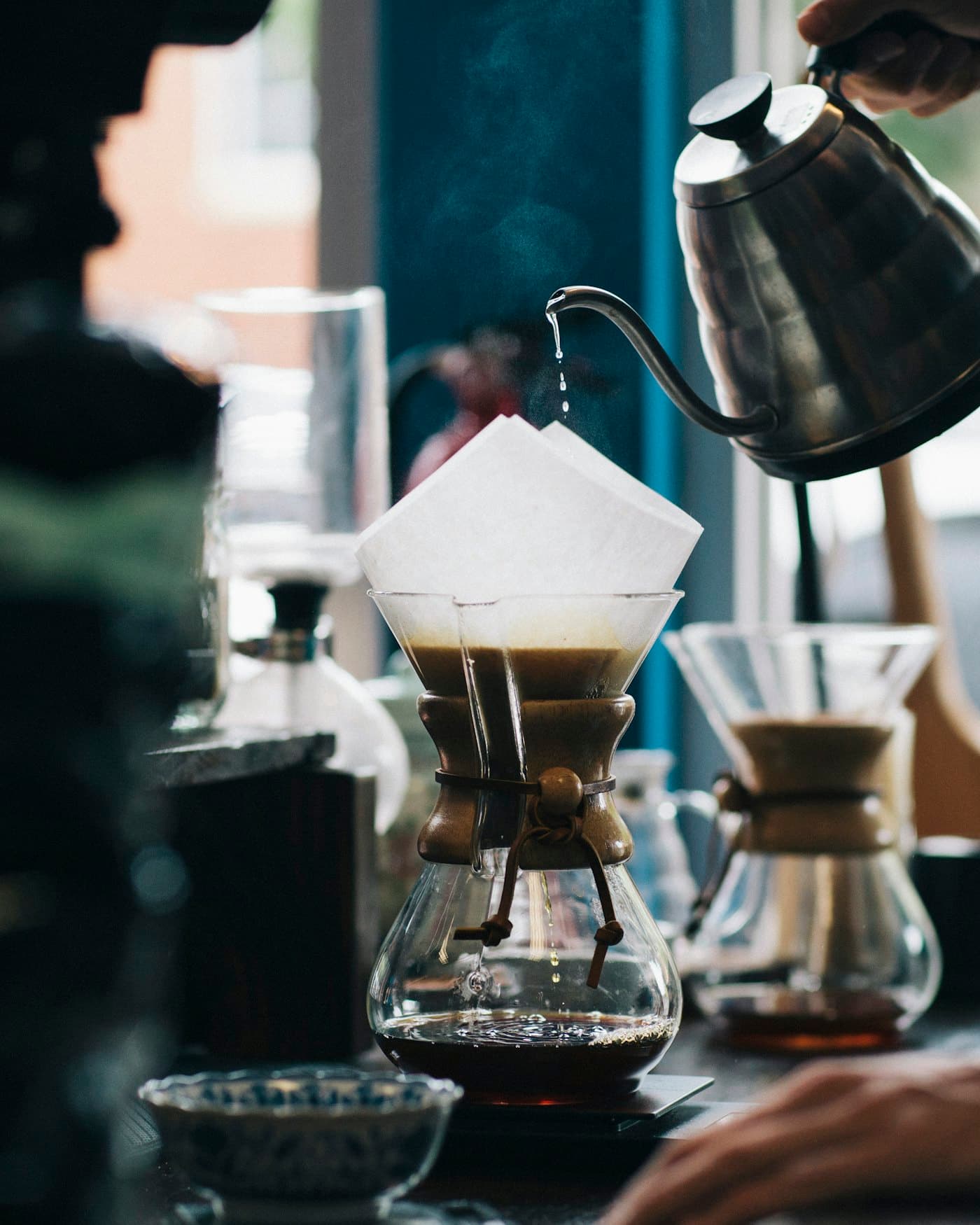 Gooseneck kettle pouring hot water over a paper filter into a glass pour-over brewer