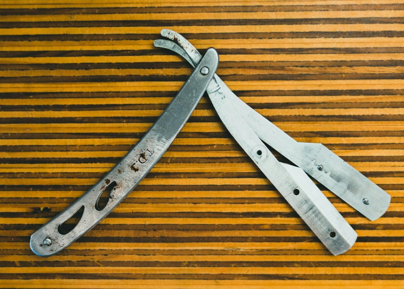 Two well-used straight razors laid open on striped wood