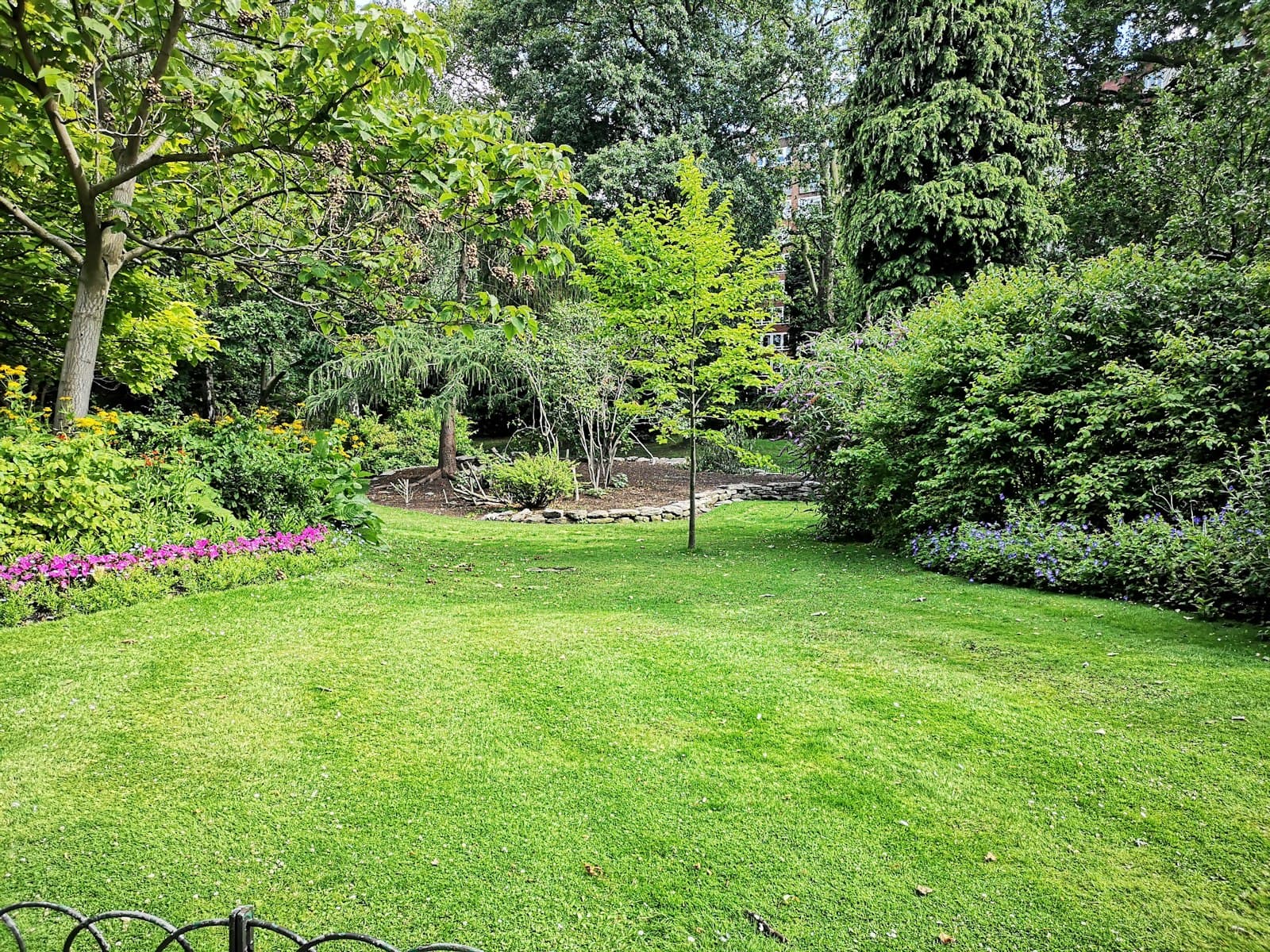 A mown lawn framed by mature planting beds
