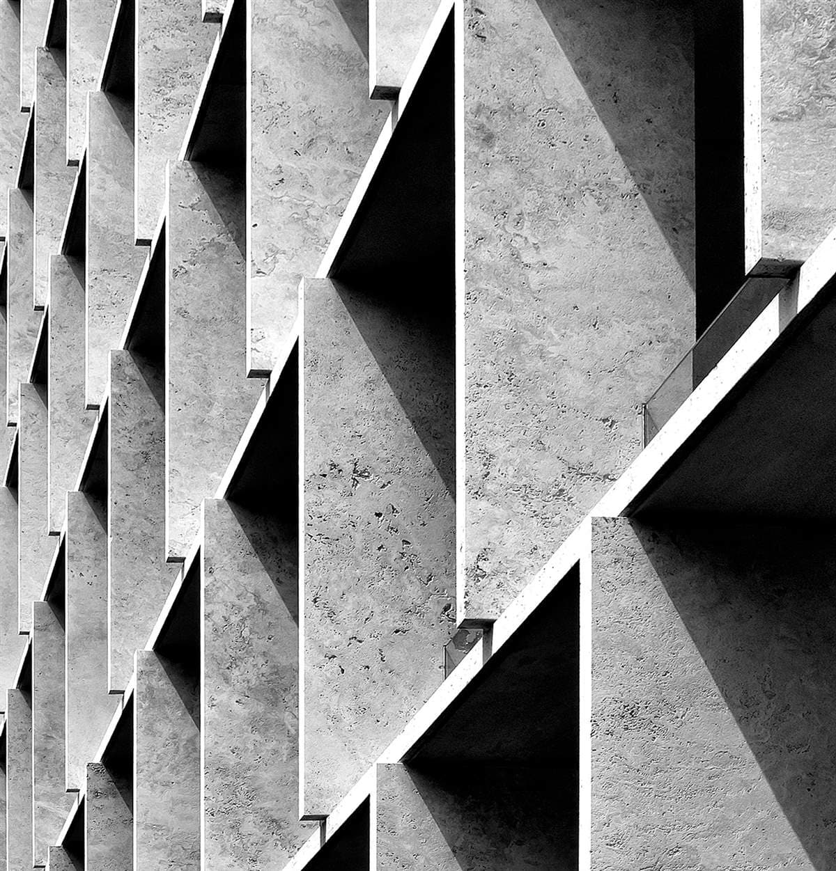 Repeating angled stone fins casting triangular shadows across a facade