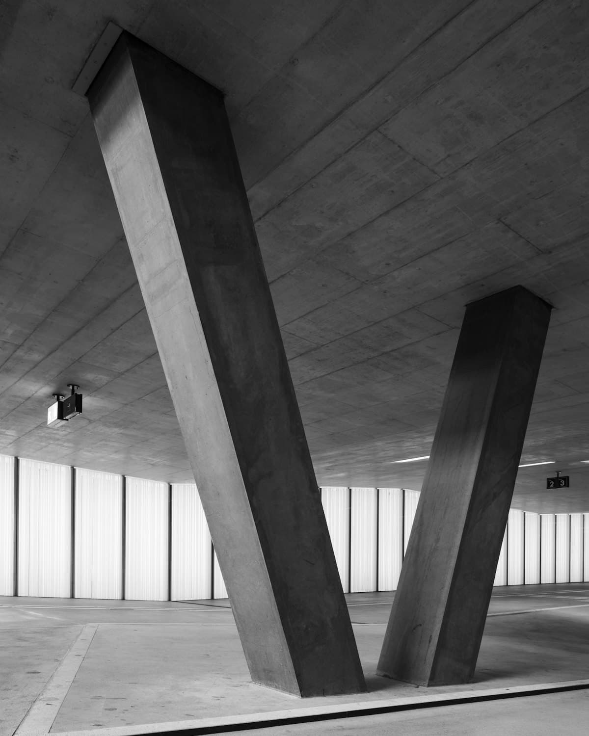 Concrete interior with V-shaped columns in front of a light-diffusing translucent wall