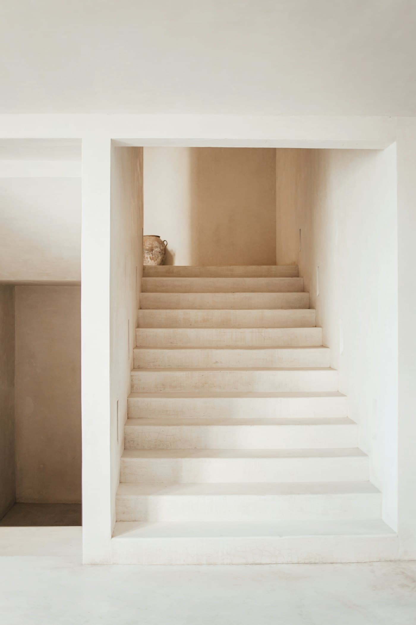 White plaster staircase rising toward a warm, softly lit landing