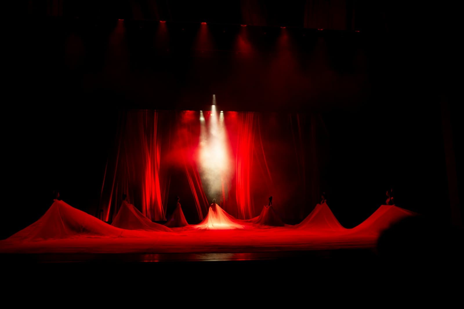 Stage washed in red light and smoke with billowing fabric under a single spotlight
