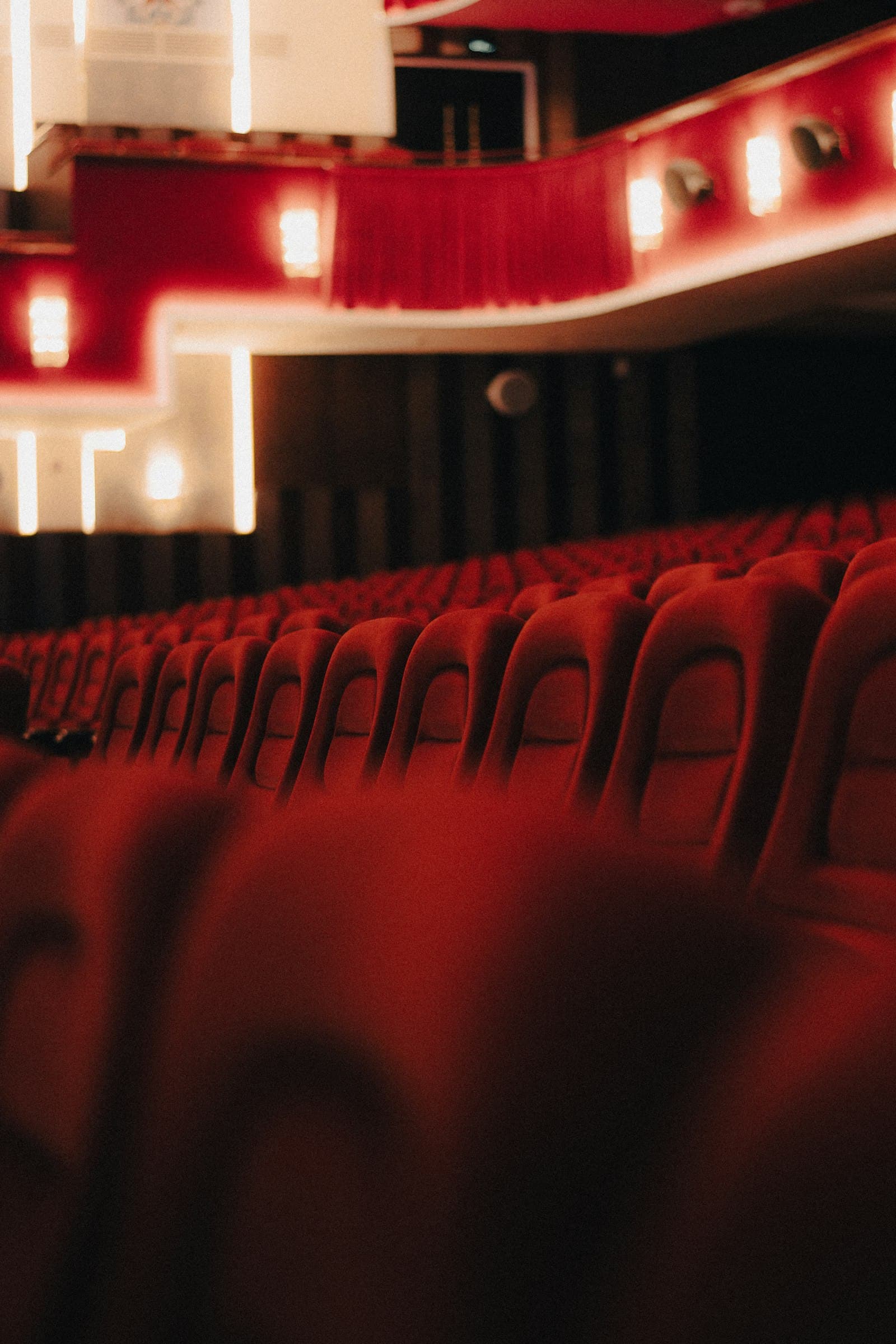 Rows of red velvet theater seats under warm balcony lights