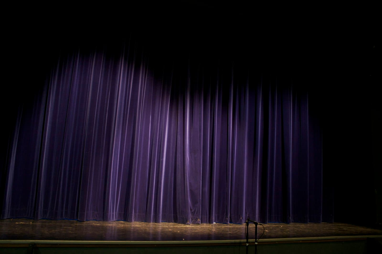 Purple velvet stage curtain lit by a spotlight with a microphone stand waiting