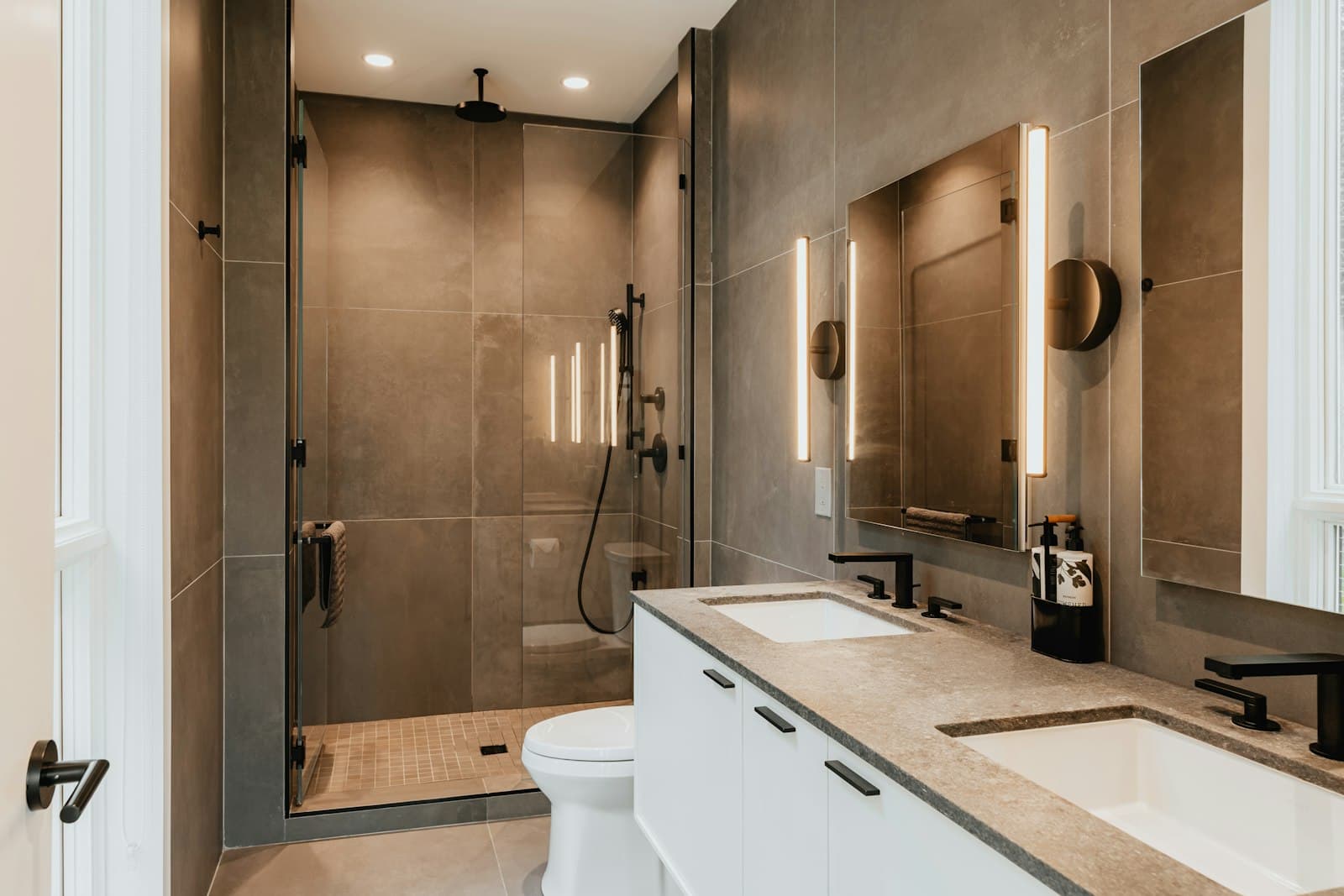 A bathroom finished in large dark tile with a glass shower