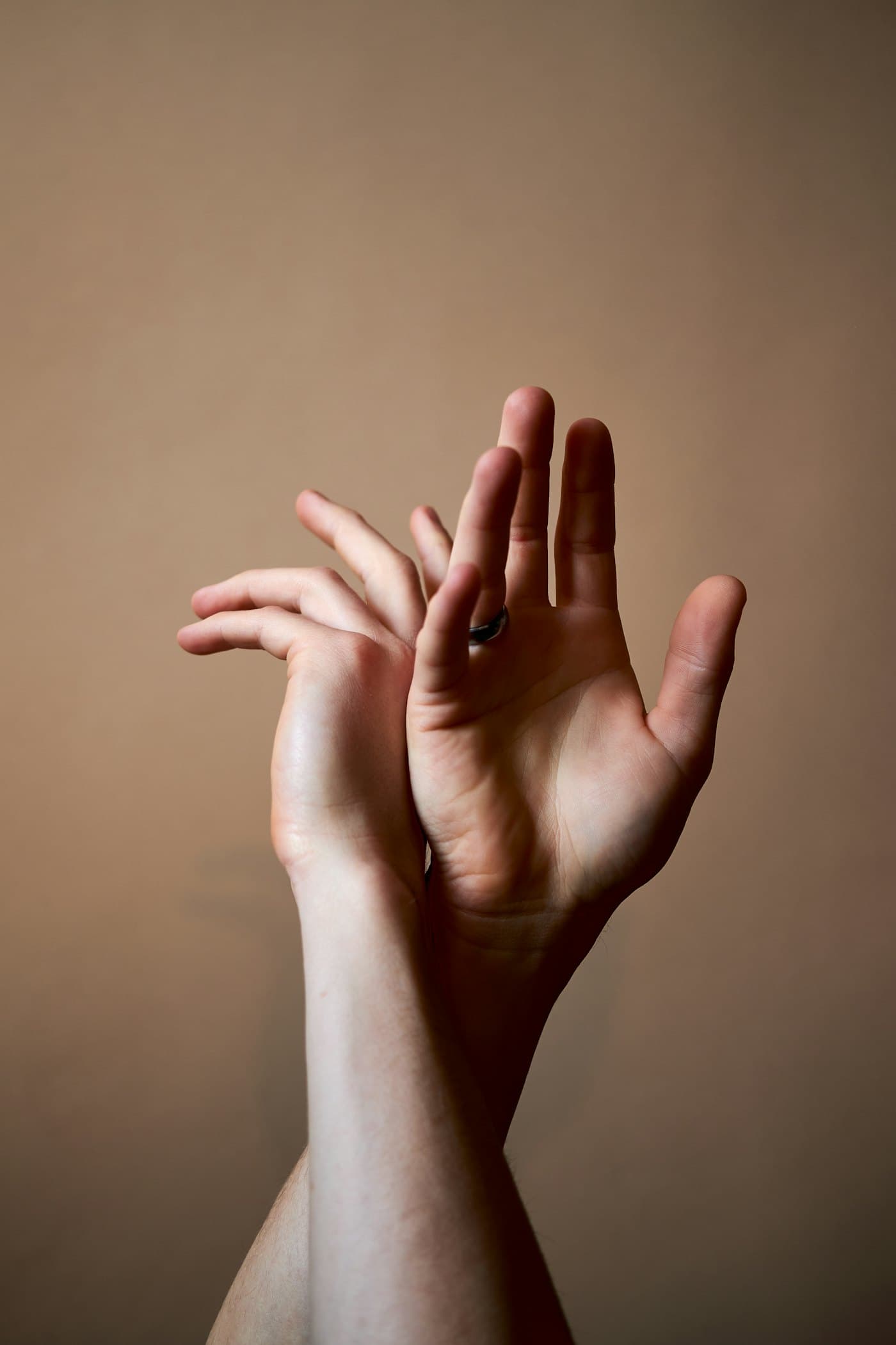 Two hands raised and gently crossed against a warm clay-colored backdrop