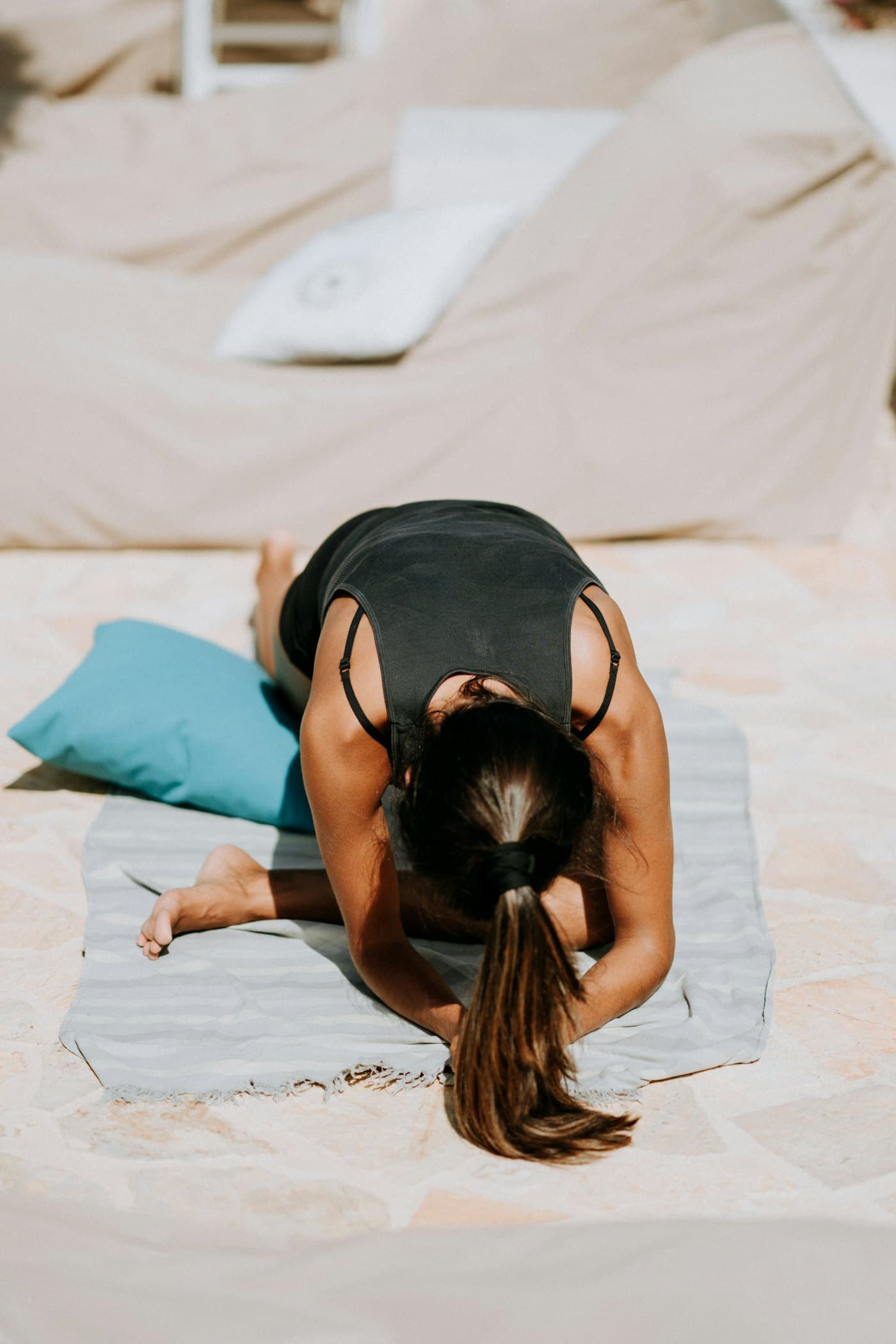 A student folded forward in child’s pose on a mat in a sunlit sandstone courtyard