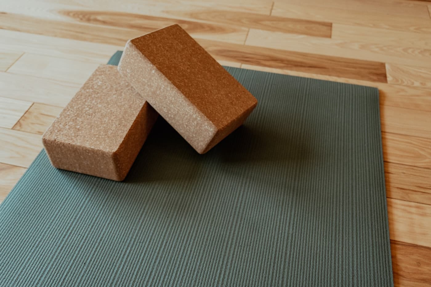 Two cork yoga blocks resting on a sage green mat on a wood floor