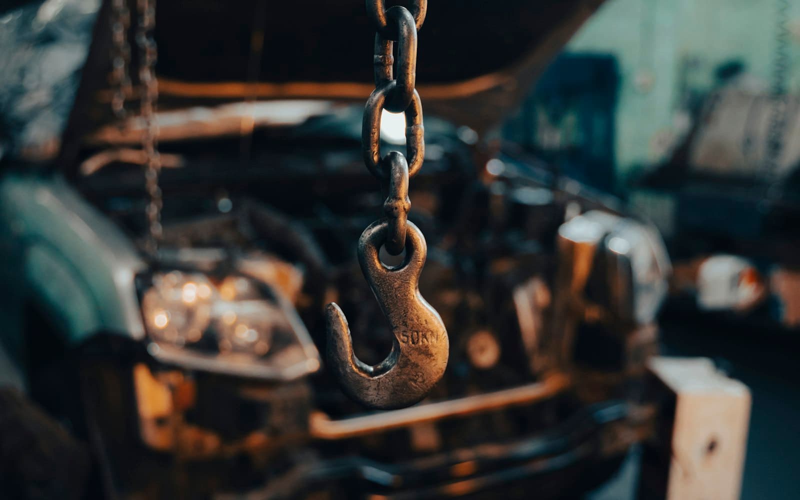 Engine hoist chain and hook over a car with its hood open in the shop
